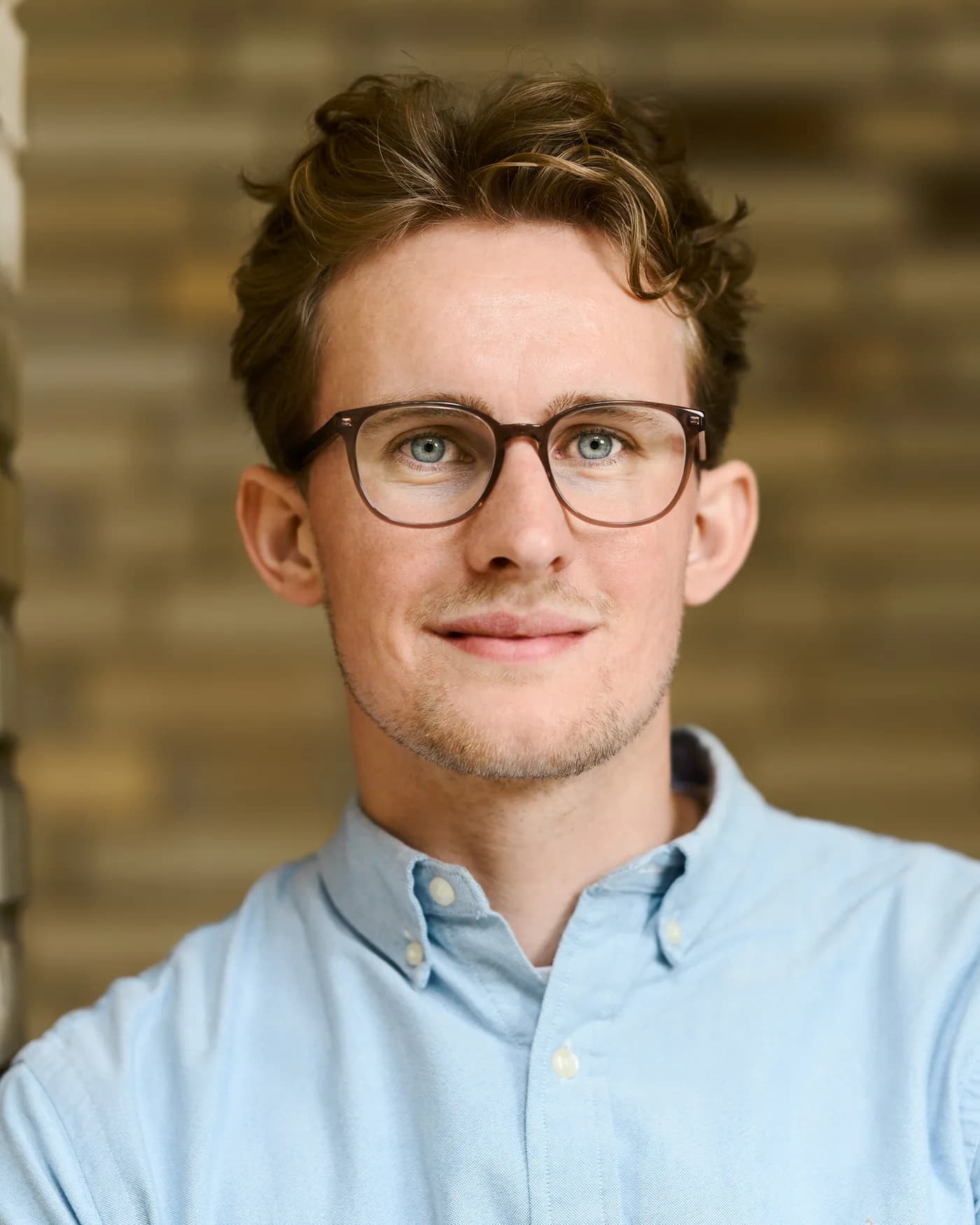 Porträt von Fabian Tiedemann mit Brille vor einer Klinkerwand